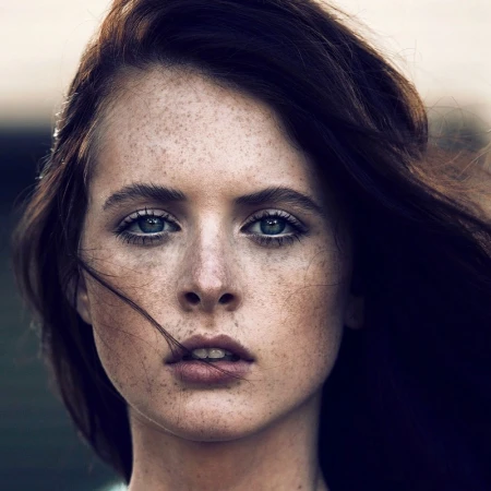 Close-up portrait of a woman with freckles and dark hair framing her face by makeup artist David Razzano