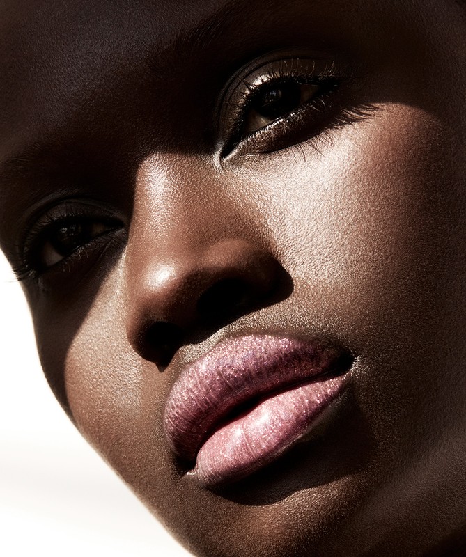 Close-up portrait of a dark-skinned woman with glossy lips, showcasing beauty and makeup artistry in natural, diffused light.