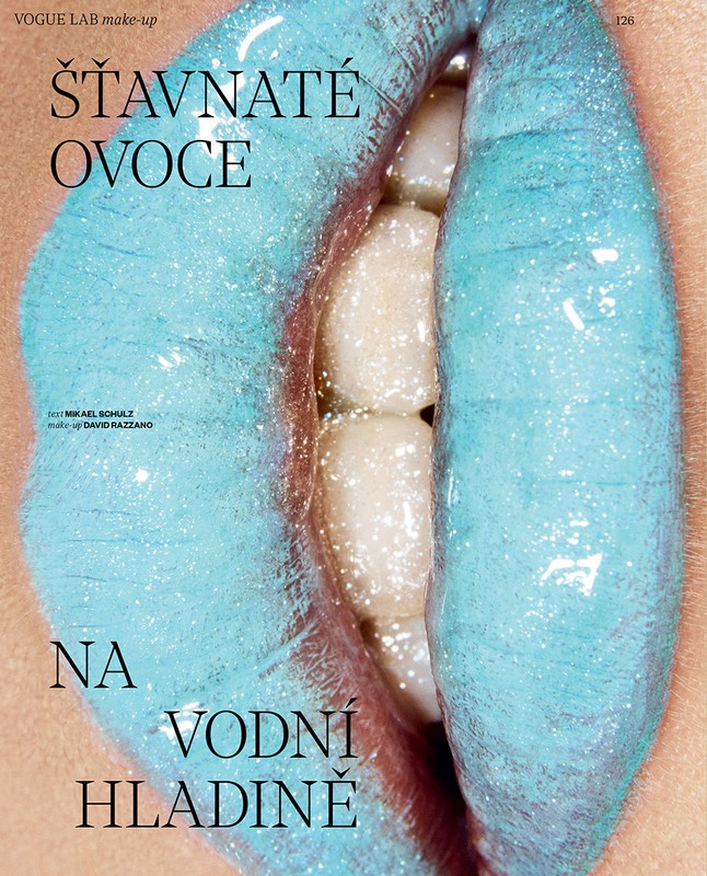 Close-up beauty shot features an adult woman with shimmery blue lipstick, partially visible teeth, and fair skin in a bright studio setting.