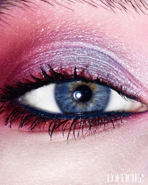 Close-up studio shot of an adult female eye with iridescent pink and silver eyeshadow, black eyeliner, and long, dark eyelashes.
