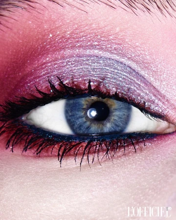 Close-up studio shot of an adult female eye with iridescent pink and silver eyeshadow, black eyeliner, and long, dark eyelashes.