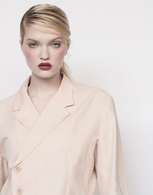 Portrait of a woman with red lipstick wearing a pale pink blazer against a plain white background