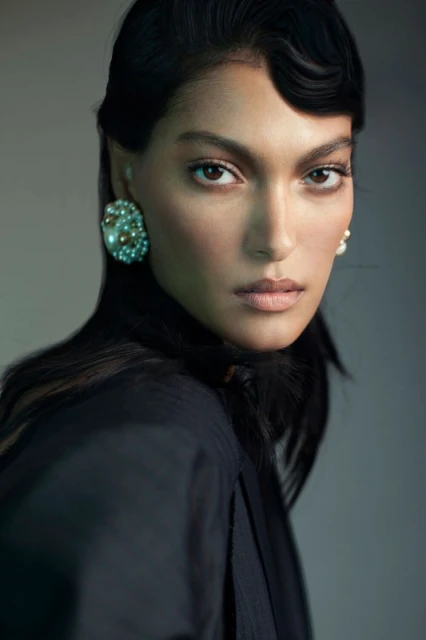 Close-up studio portrait of a woman with dark hair and pearl earrings wearing a black jacket with soft, diffused lighting.