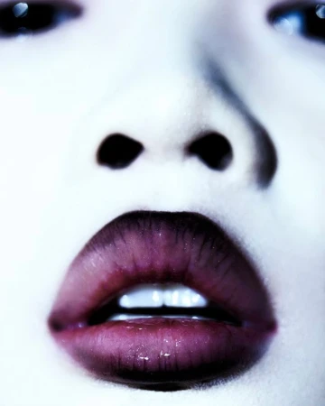 Close-up portrait of a woman with dark lined lips and white teeth by make-up artist David Razzano