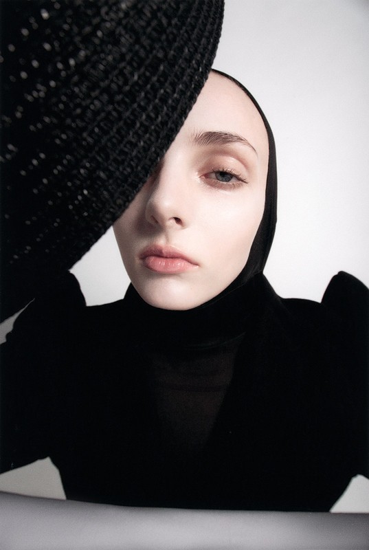 Close-up portrait of a woman wearing a black hat and turtleneck against a plain white background with make-up by David Razzano.