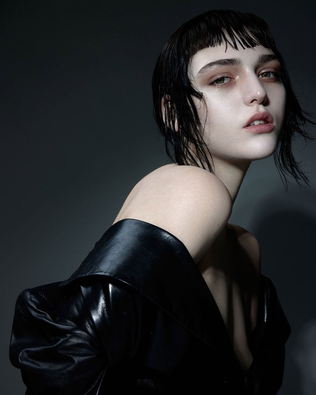 Close-up portrait of a woman with wet dark hair, micro bangs, and make-up by David Razzano against a dark gradient background