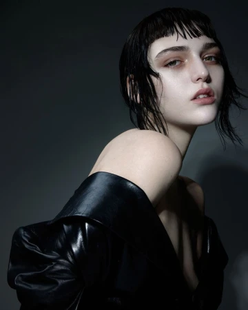 Close-up portrait of a woman with wet dark hair, micro bangs, and make-up by David Razzano against a dark gradient background