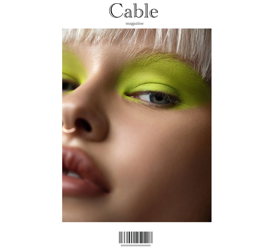 Close-up of a woman with blonde hair and bright green eye makeup on the cover of Cable magazine, showcasing a vivid beauty style.