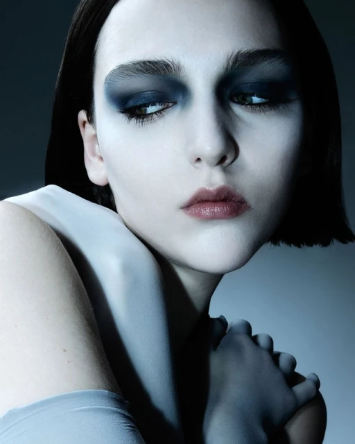 Striking beauty shot of a young adult woman with dark hair and dramatic eye makeup in cool lighting, highlighting fashion and portrait elements.