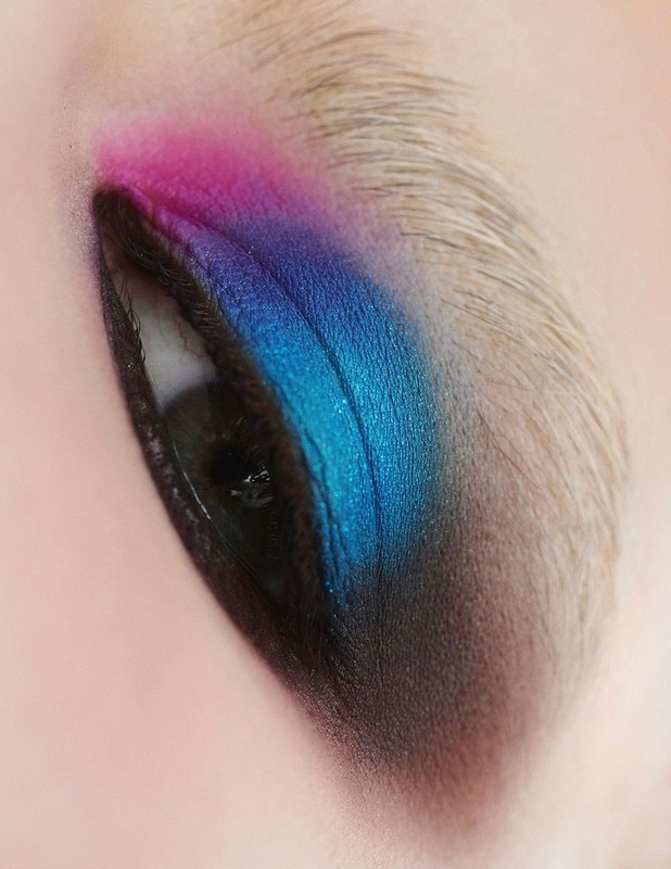 Close-up of a human eye with vibrant pink, blue, and black eyeshadow, showcasing a blend of colors and detailed makeup application.