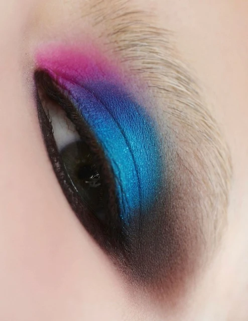 Close-up of a human eye with vibrant pink, blue, and black eyeshadow, showcasing a blend of colors and detailed makeup application.