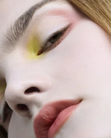 Close-up portrait of a model with artistic makeup featuring yellow eyeshadow, pink accents, and muted rose lipstick by David Razzano.