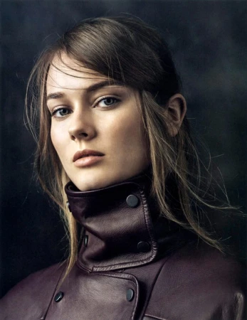 Portrait of a young woman with brown hair wearing a dark plum leather high-neck jacket against a textured dark background.