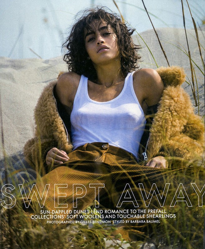 Model with dark curly hair wearing a white tank top and corduroy trousers reclining among sand dunes