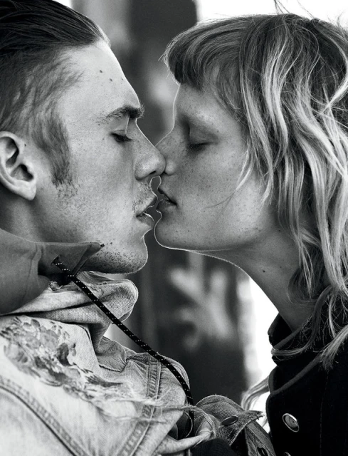 Black and white portrait of a couple kissing with a shallow depth of field. The male figure wears a jean jacket.