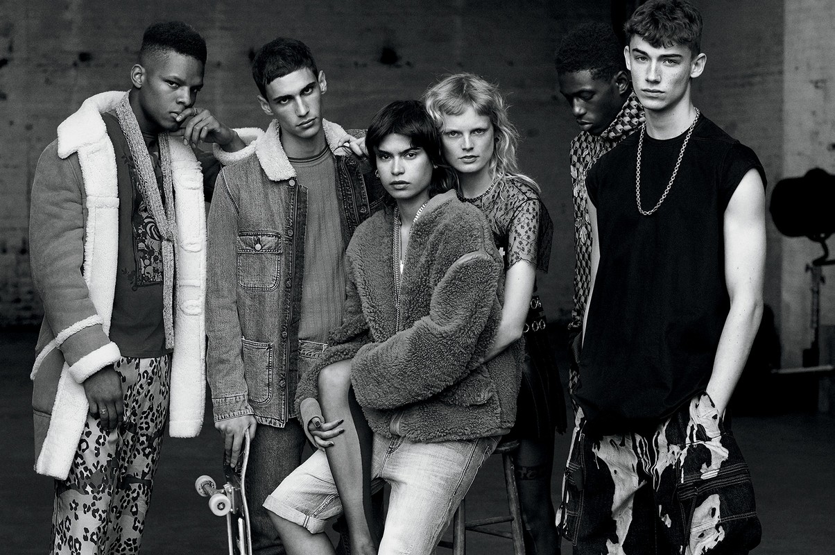 Group of six fashion models in monochromatic studio shot showcasing diverse outerwear and casual streetwear against a neutral backdrop.