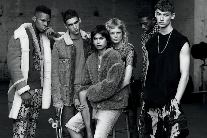 Group of six fashion models in monochromatic studio shot showcasing diverse outerwear and casual streetwear against a neutral backdrop.