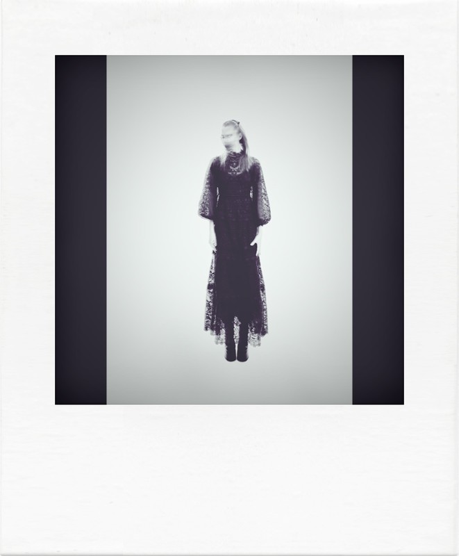 Monochromatic fashion shot featuring a woman in a long, dark, lace dress against a pale background, framed by a black vertical bar.