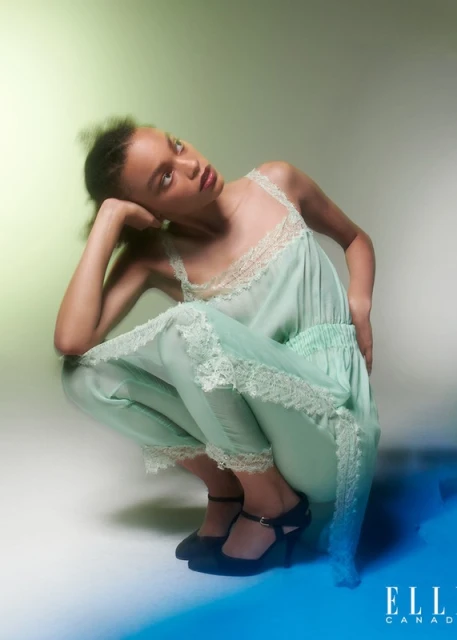 Young woman in light blue camisole set poses in a studio, head tilted with hand near face. Black shoes and ELLE Canada logo visible.