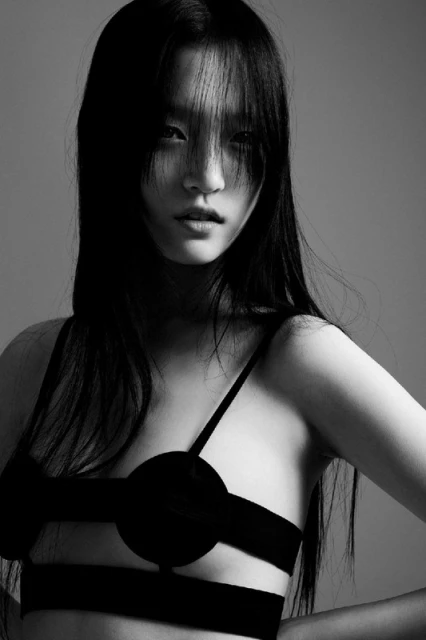 Close-up of a black and white portrait of a woman with long dark hair posing in an open bustier top against a gray background.