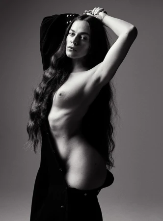 Black-and-white portrait of a slender woman with long wavy hair, partially unclothed, posing against a neutral background, creating a dramatic effect.
