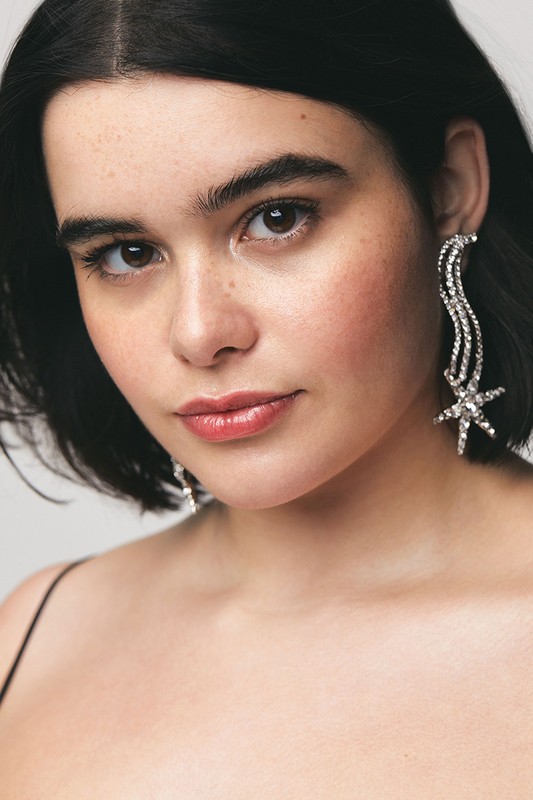 Close-up portrait of a woman with short, dark hair wearing crystal starburst earrings against a neutral background, fashion, beauty.