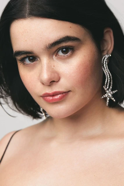 Close-up portrait of a woman with short, dark hair wearing crystal starburst earrings against a neutral background, fashion, beauty.