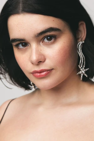 Close-up portrait of a woman with short, dark hair wearing crystal starburst earrings against a neutral background, fashion, beauty.