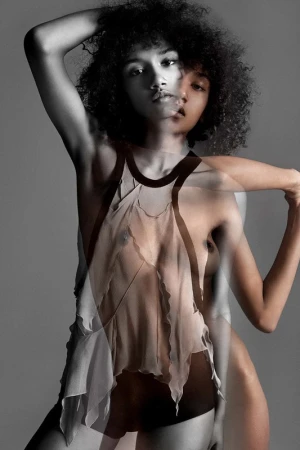 Multiple exposure portrait of a woman with curly hair wearing a sheer layered top against a grey studio backdrop.