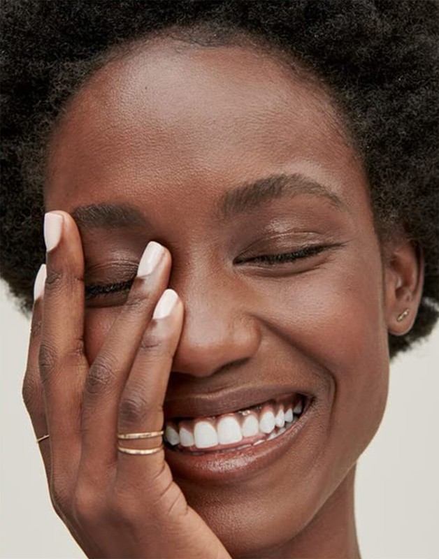 Close-up portrait of a smiling Black woman with short afro hair touching her face with manicured white nails.