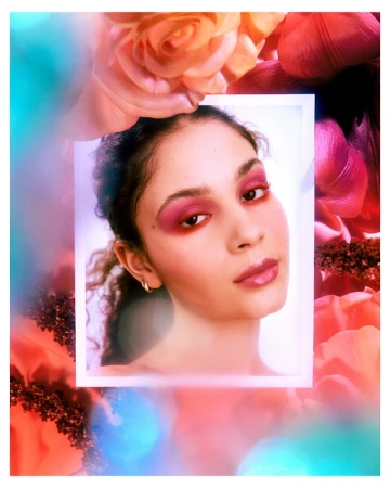 Close-up portrait of a young woman with pink eye shadow and glossy lips, surrounded by soft-focus floral elements.