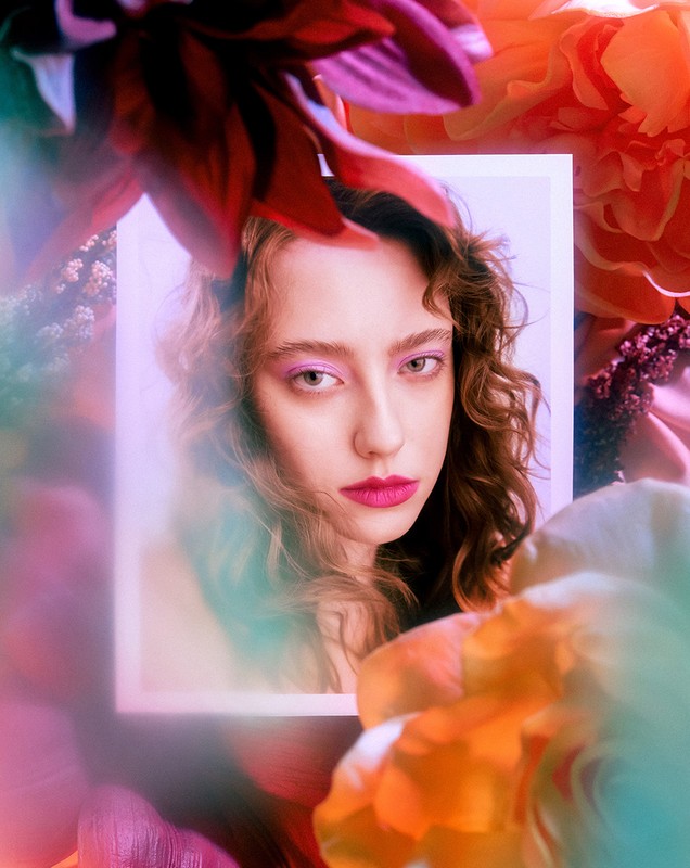 Portrait of a woman with curly hair framed by colorful floral elements and soft prismatic lighting effects