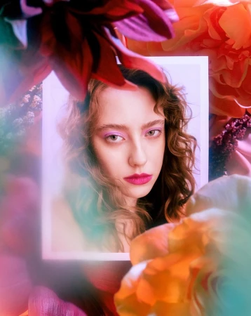 Portrait of a woman with curly hair framed by colorful floral elements and soft prismatic lighting effects
