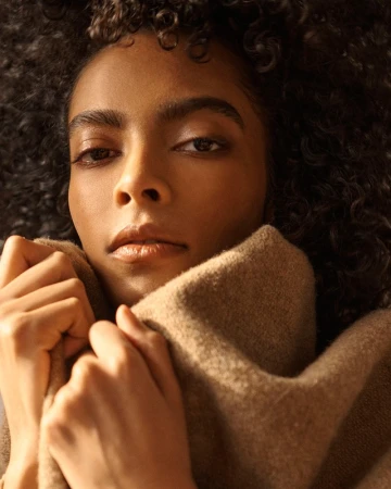 Close-up portrait of a woman with curly hair pulling up a high-collared camel wool coat against her chin.