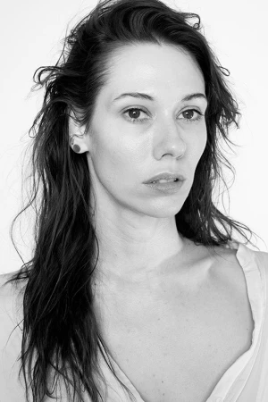 Portrait of a woman with dark wavy hair and earrings against a plain white background by Destiny Venice