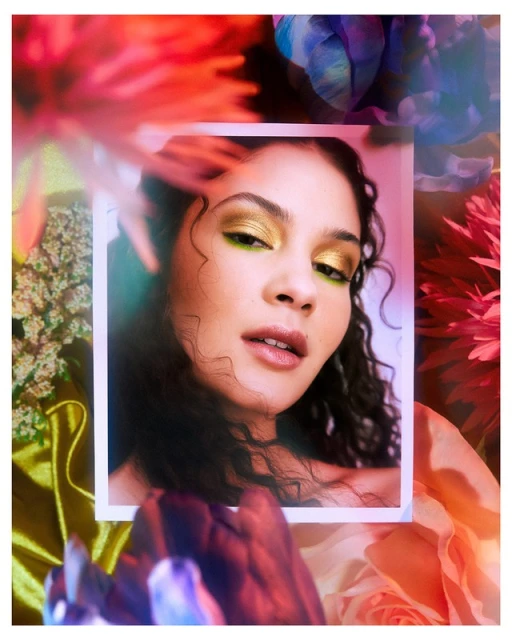 Portrait of a young woman with gold eyeshadow framed by flowers in a photo-shoot style; beauty and fashion concept; close-up.