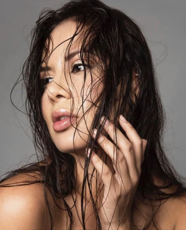 Close-up beauty portrait of a woman with wet dark hair touching her face against a neutral grey background