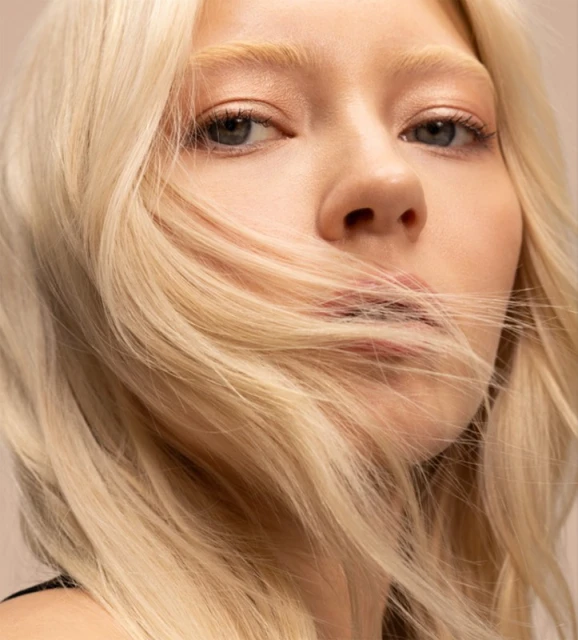 Close-up portrait of a young adult woman with light blonde hair, showcasing beauty and fashion in a studio setting with a neutral backdrop.