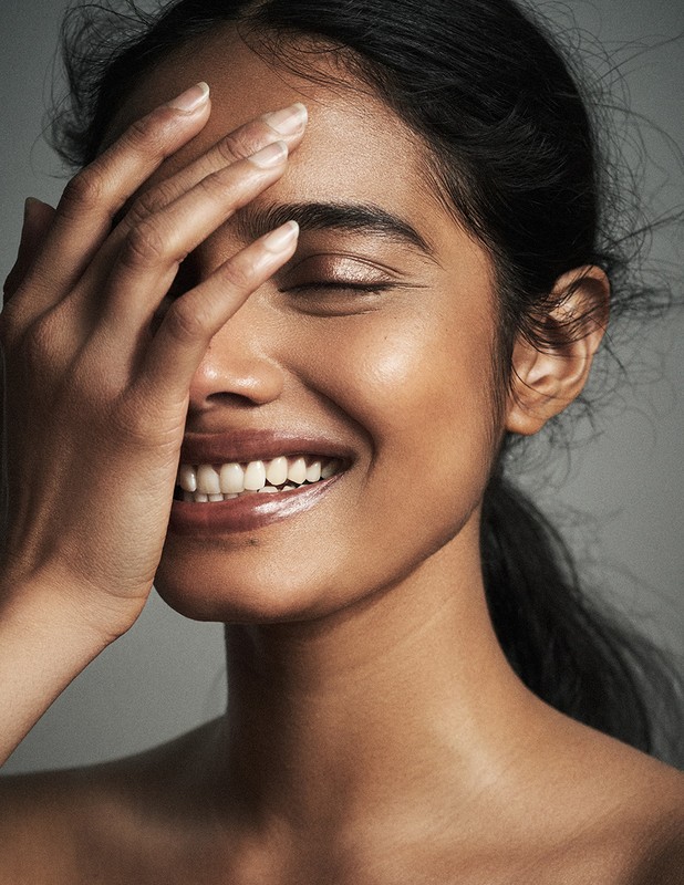 Close-up portrait of a smiling South Asian woman with her hand covering part of her face, styled by Destiny Venice.