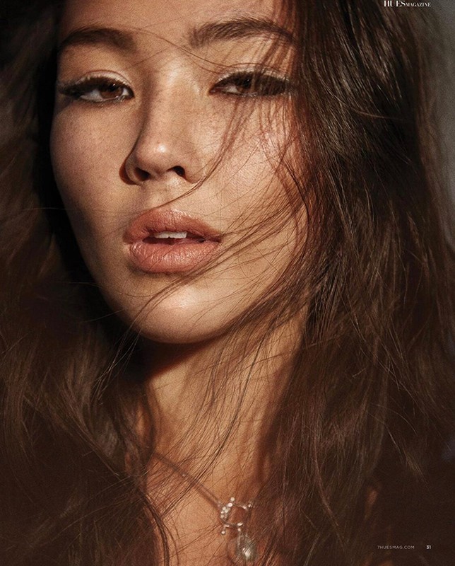 Close-up portrait of an adult female with long, dark hair, wearing a necklace, with light makeup and sunlight hitting her face.