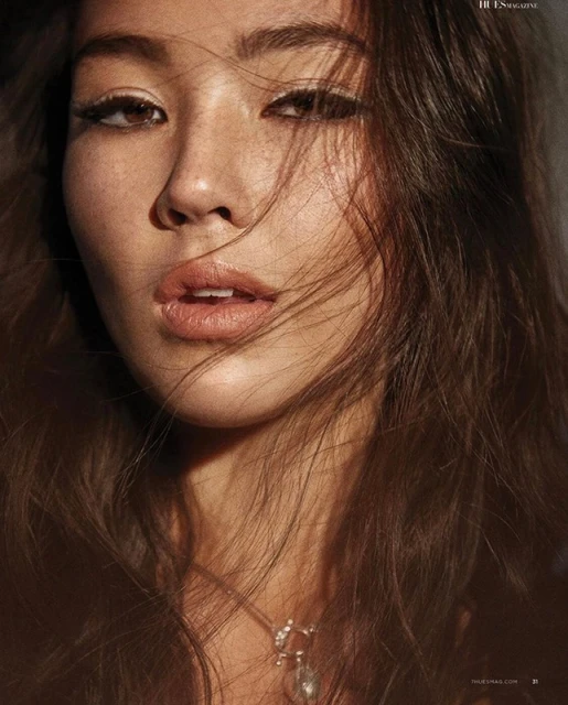 Close-up portrait of an adult female with long, dark hair, wearing a necklace, with light makeup and sunlight hitting her face.