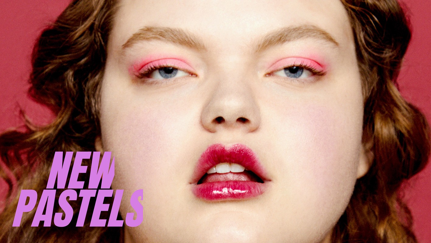 Close-up of a young adult woman with pink eyeshadow and shiny dark pink lipstick against a light pink background.