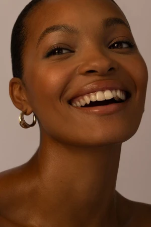 Close-up portrait of a smiling Black woman wearing gold hoop earrings with hair styled by Destiny Venice.