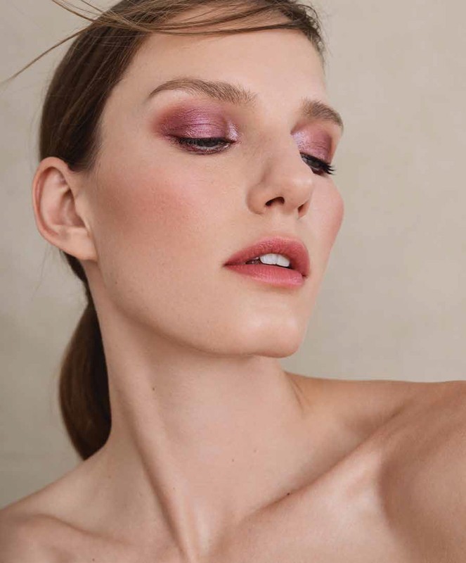 Close-up portrait of a woman with metallic pink eyeshadow and mauve lips against a neutral background.