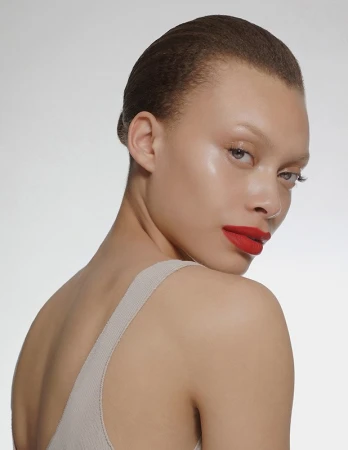 Close-up portrait of a woman with red lipstick and slicked-back hair against a neutral background
