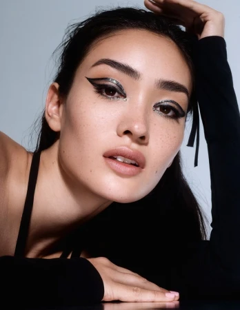 Close-up portrait of a woman with dramatic black winged eyeliner, rhinestone accents, and dark hair styled by Destiny Venice.