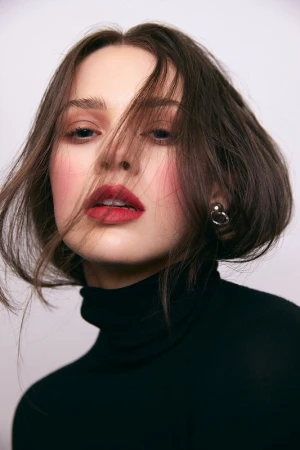 Close-up portrait of a woman with short dark hair wearing a black turtleneck against a plain white background