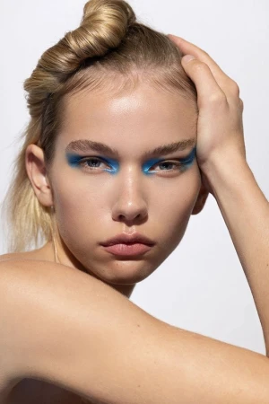 Close-up beauty portrait of a model with blue eye makeup and styled blonde hair by Destiny Venice against a white background