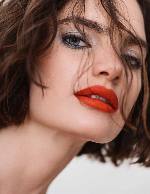 Close-up portrait of a woman with red lipstick, smoky eye makeup, and brunette hair on a white background, beauty shot.