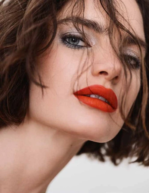 Close-up portrait of a woman with red lipstick, smoky eye makeup, and brunette hair on a white background, beauty shot.